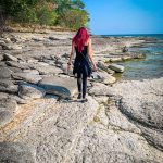 Femme marchant sur des roches au bord de l’eau, de dos, dans un paysage naturel, symbolisant la connexion à soi et à la nature