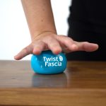 Main exerçant une pression sur la balle Twist Fascia posée sur une table, illustrant une technique de massage des fascias.